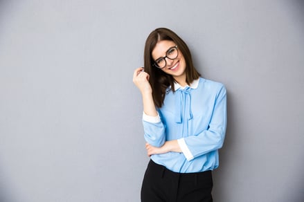 Smiling businesswoman in glasses standing over gray background. Wearing in blue shirt and glasses. Looking at camera