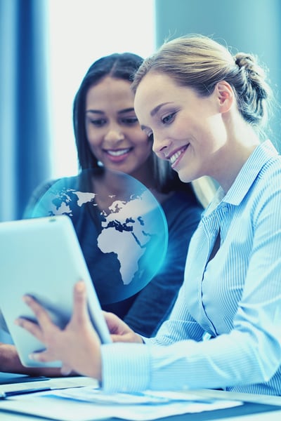 2 professional women looking at a tablet with a hologram of a globe 2 professional women looking at a tablet with a hologram of a globe