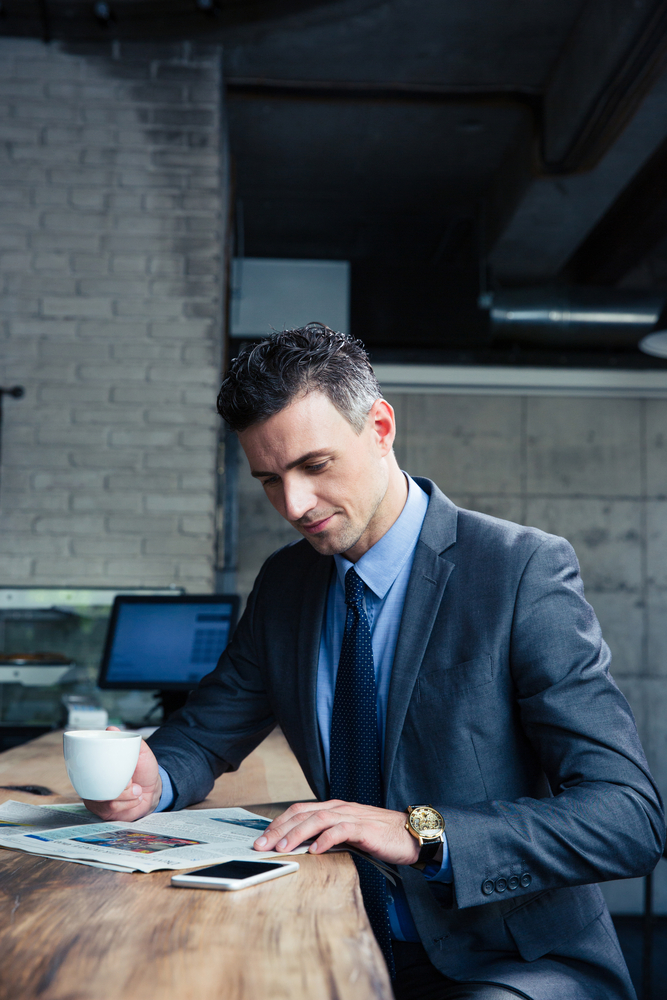 Confident businessman reading magazine and drinking coffee in cafe